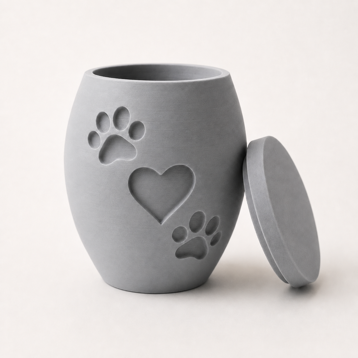 Light gray 3D printed pet memorial urn with heart and two paw print design, lid removed.