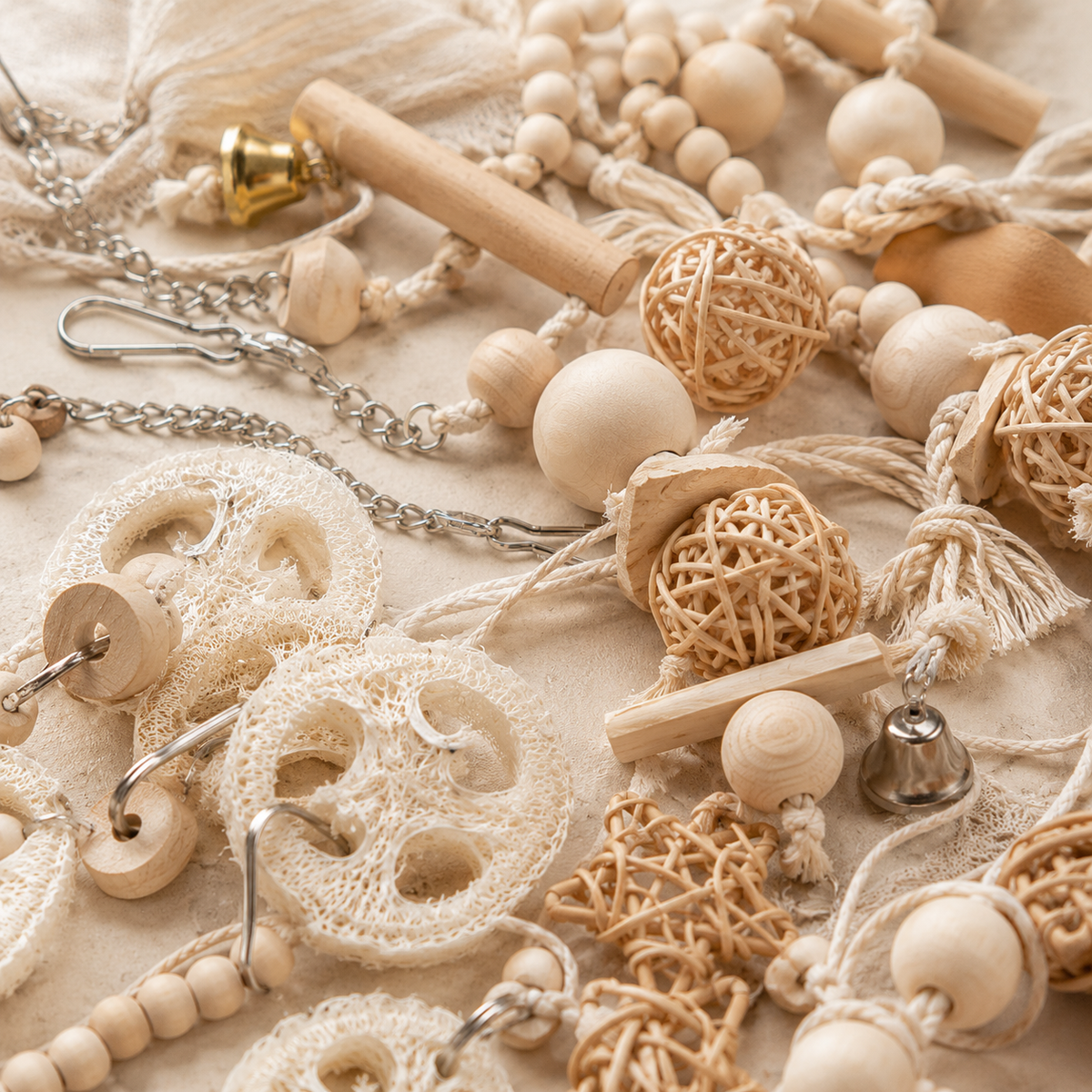 Close-up detail of mixed bird toy set pieces including loofah slices, woven rattan balls, wooden beads, a brass bell and metal chain and clips.