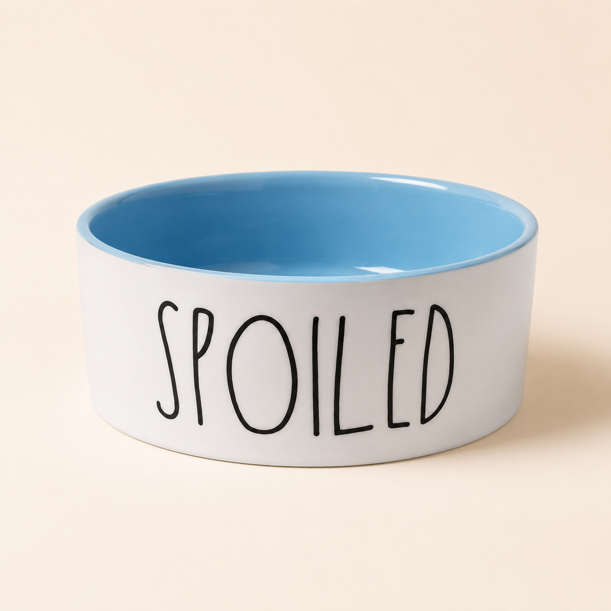 Blue and white Spoiled ceramic pet bowl with glossy blue interior and black lettering on a cream background.