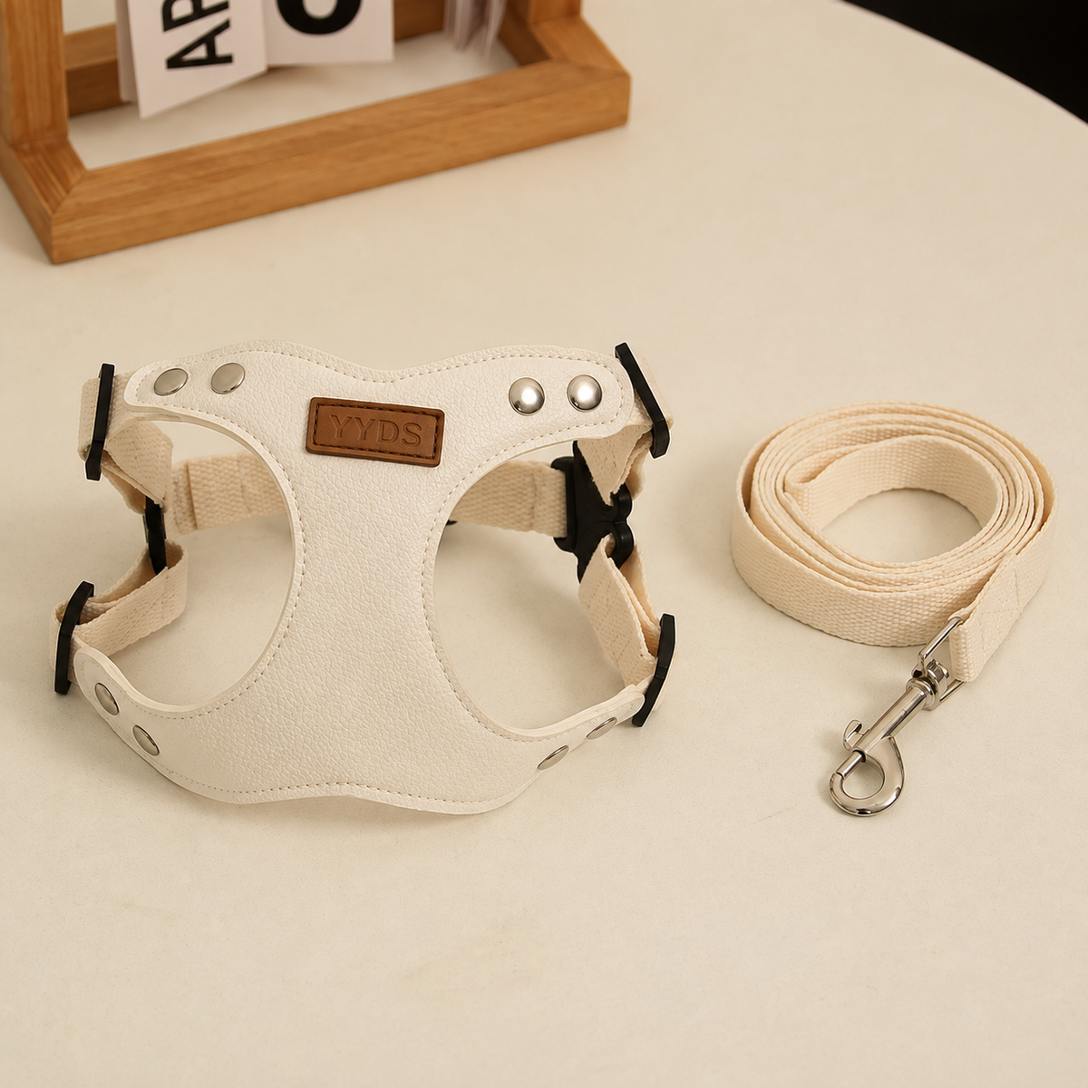 Ivory leather YYDS pet harness and matching leash arranged on a warm neutral tabletop in a premium product presentation.