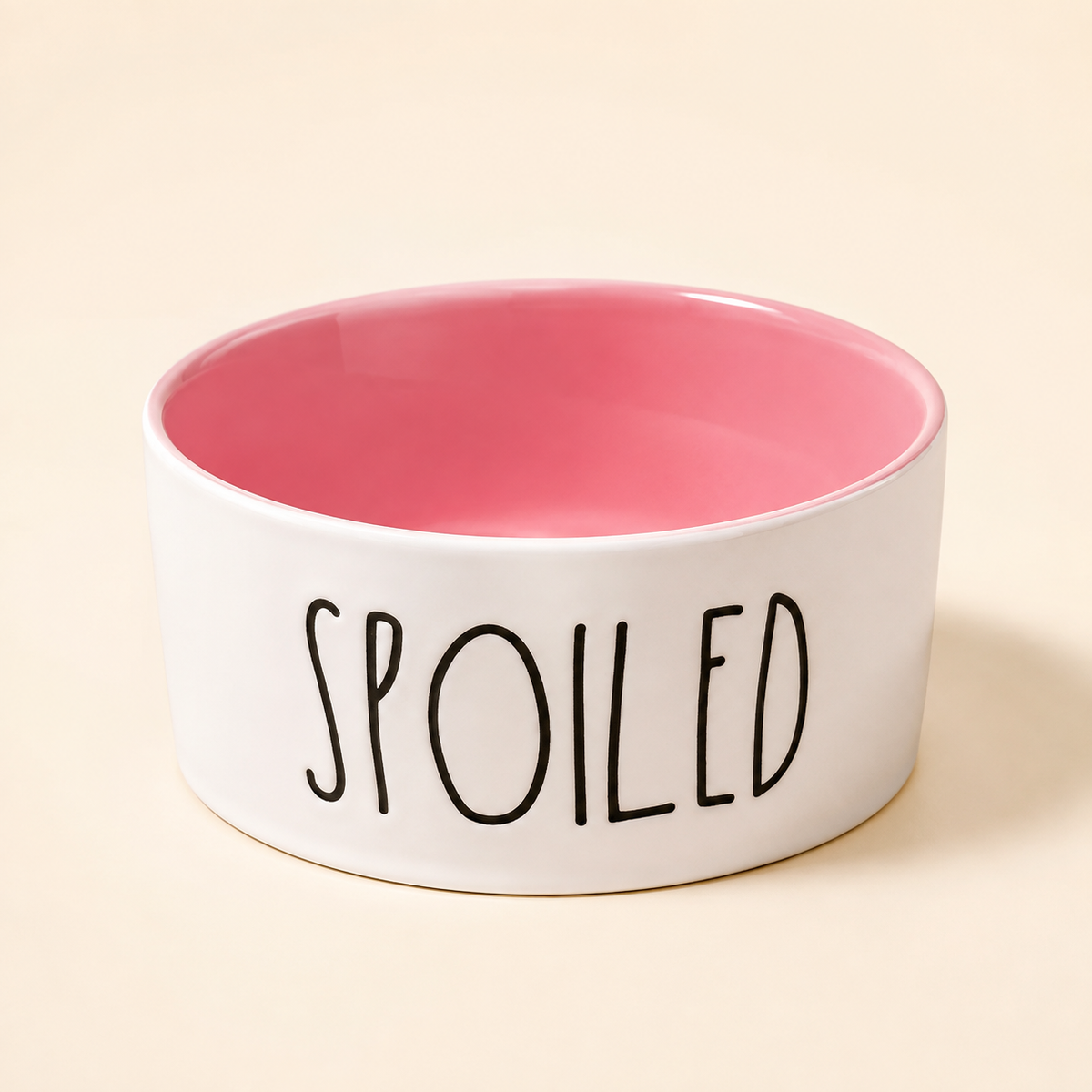 Pink and white Spoiled ceramic pet bowl with glossy pink interior and black lettering on a warm neutral background.