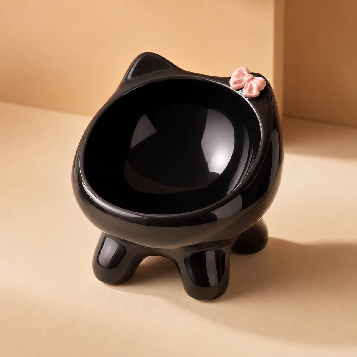Elevated glaze black ceramic cat bowl with rounded feet and a pink bow accent on a warm neutral background.