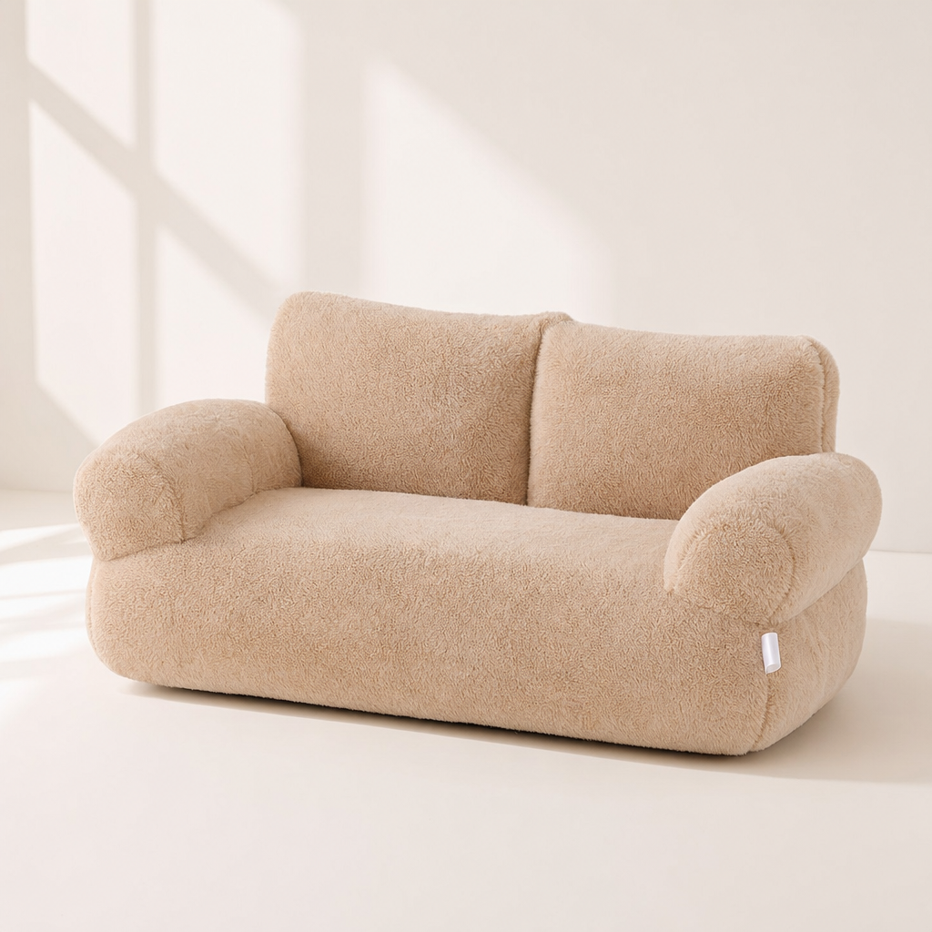 A latte beige plush cat bed shaped like a small sofa, with a two-part backrest and rounded armrests.