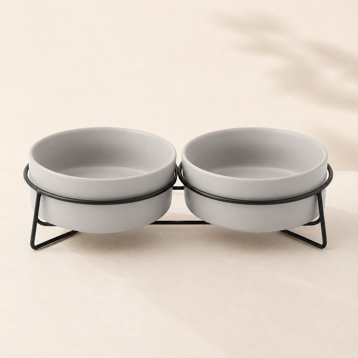 Double elevated gray ceramic pet bowls in a black metal stand on a refined neutral background.