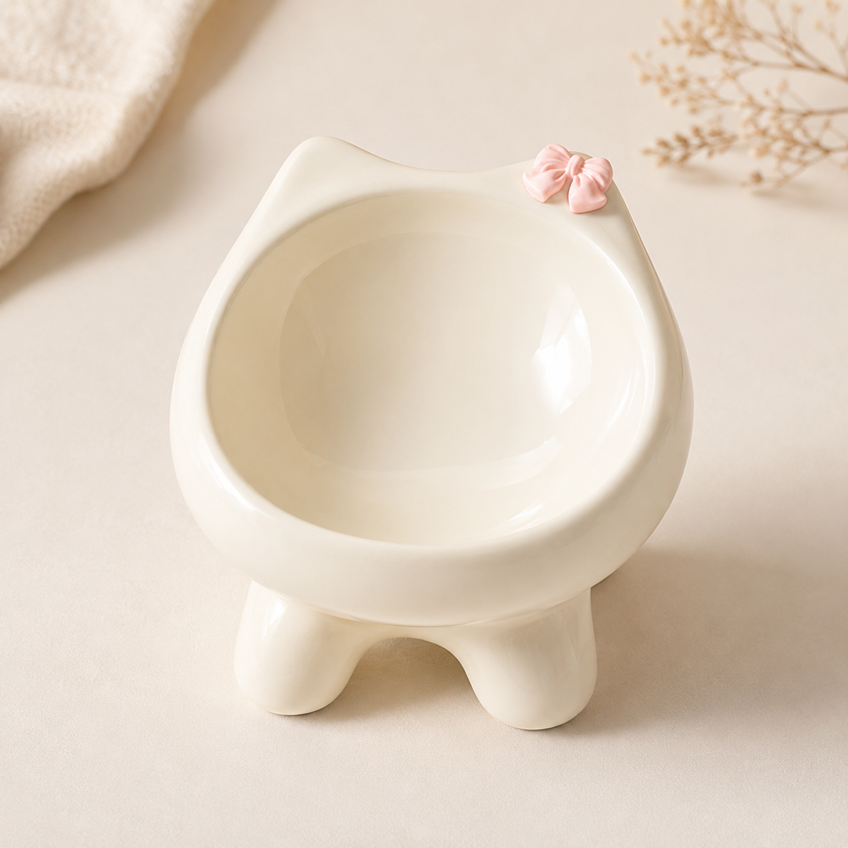 Elevated off-white ceramic cat bowl with rounded feet and a pink bow accent in a clean studio-style product shot.